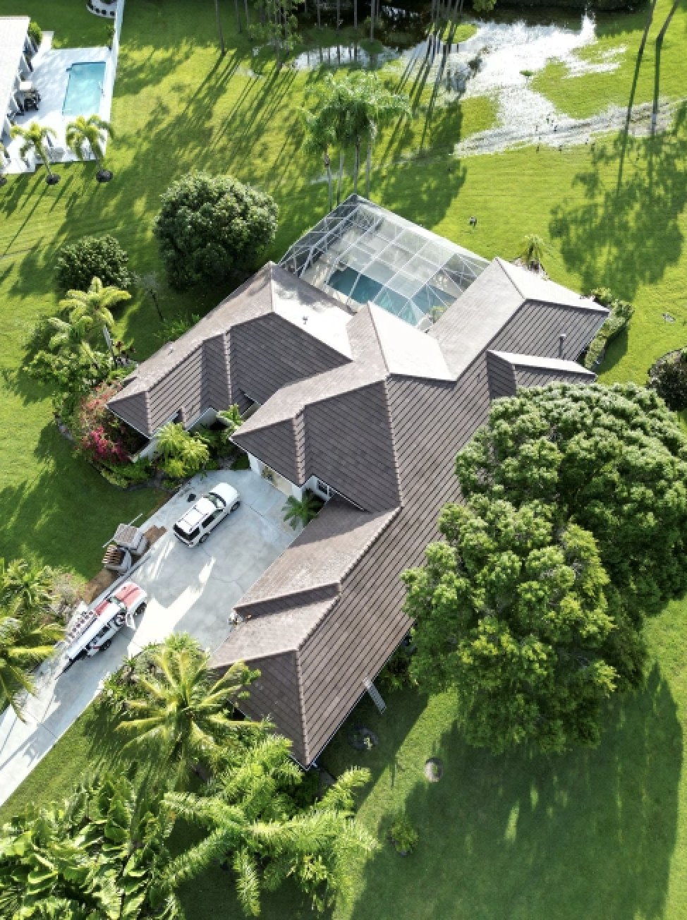Aerial of a brown architectural shingle roof on a Lutz home with a screened pool cage and crew trucks