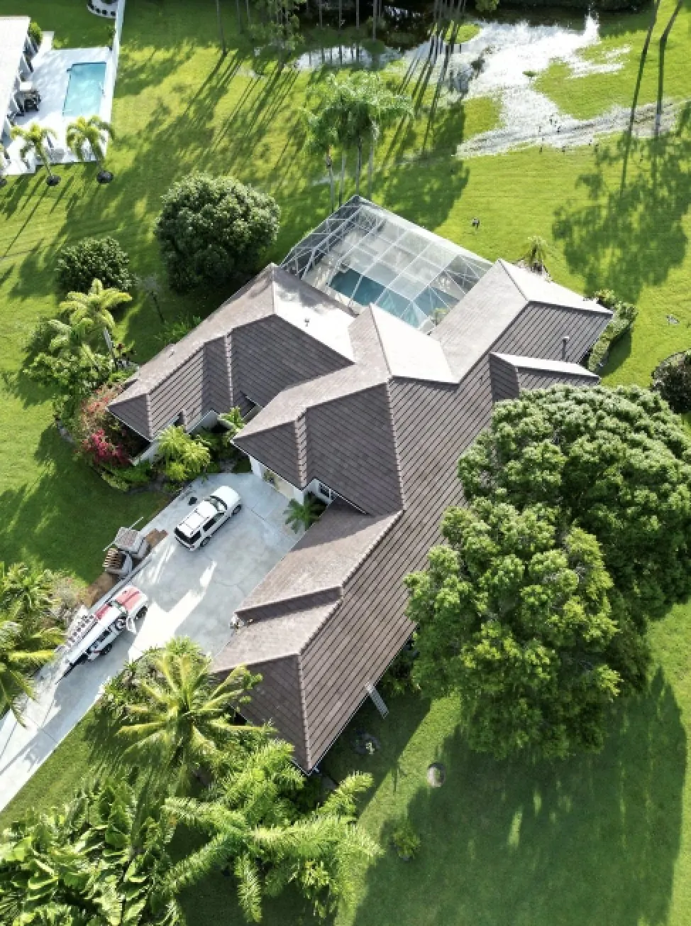 Aerial of a brown architectural shingle roof on a Lutz home with a screened pool cage and crew trucks