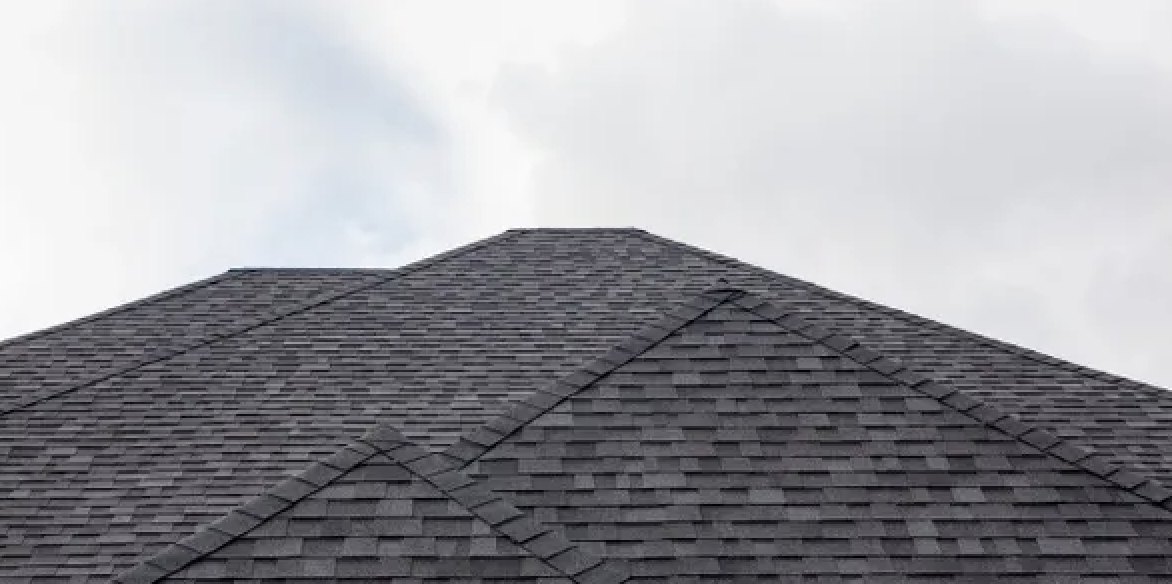 Low-angle view of dark architectural shingle hips and ridge against a cloudy Florida sky