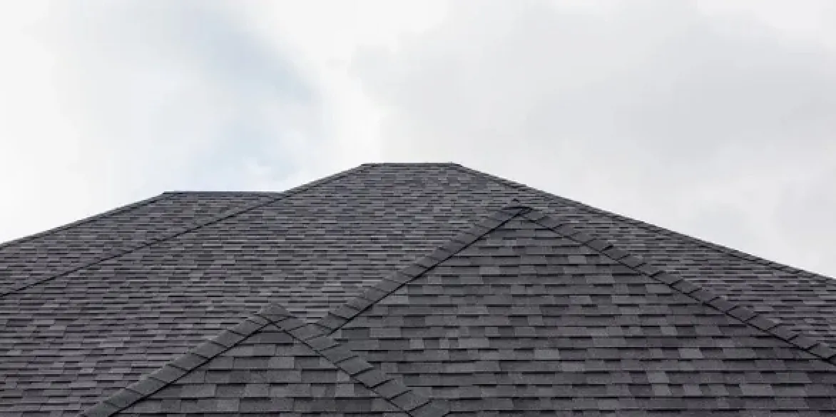 Low-angle view of dark architectural shingle hips and ridge against a cloudy Florida sky