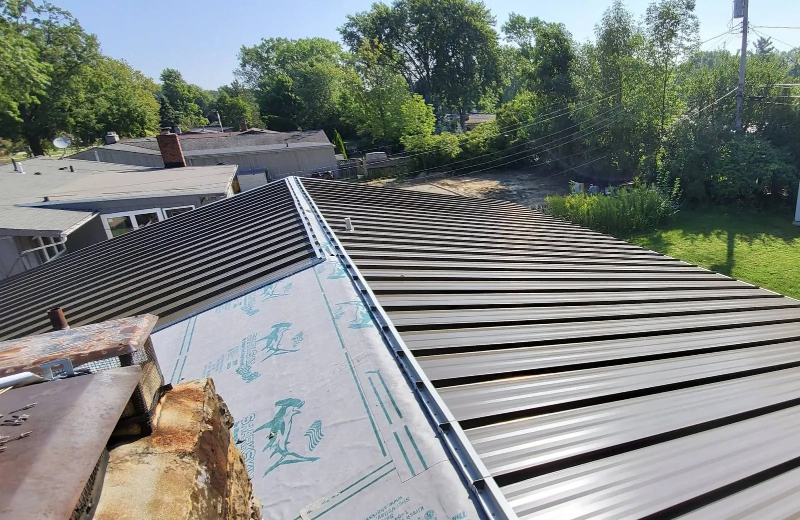 Standing-seam metal roof installation in Plant City with underlayment still exposed at the chimney